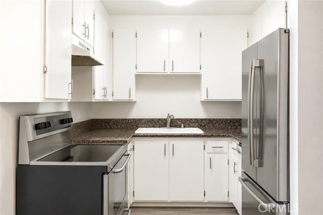 A clean, modern kitchen with white cabinets, speckled dark countertops, and stainless steel appliances.