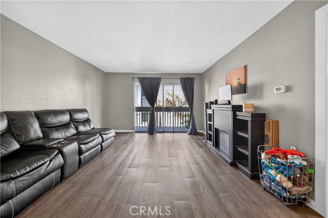 Spacious living room with gray walls, wood-look flooring, a large black leather reclining sofa, and a black fireplace mantel unit.