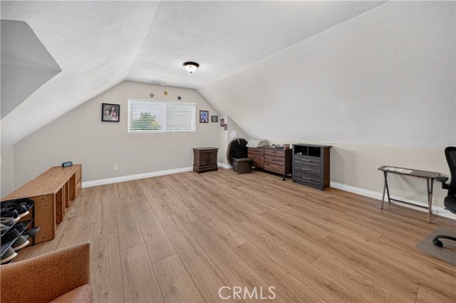 A finished attic room with light-colored walls, sloped ceilings, and wood-look laminate flooring, featuring various furniture pieces including dressers and a desk.