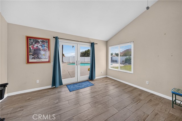 Spacious living room with wood-look tile flooring, vaulted ceilings, and glass french doors leading to a backyard pool area.