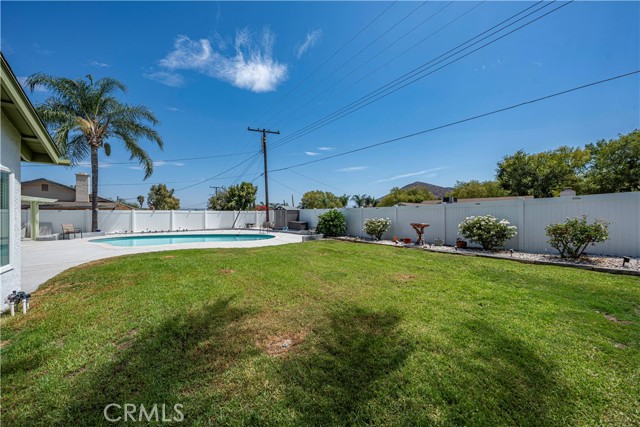 A backyard featuring a swimming pool, green lawn, and a white privacy fence under a blue sky.