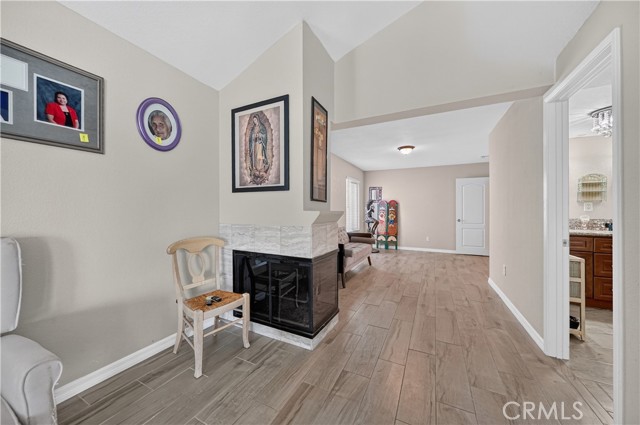 A living room area featuring a fireplace with tiled surround, wood-look tile flooring, and a view into a hallway and adjacent room.
