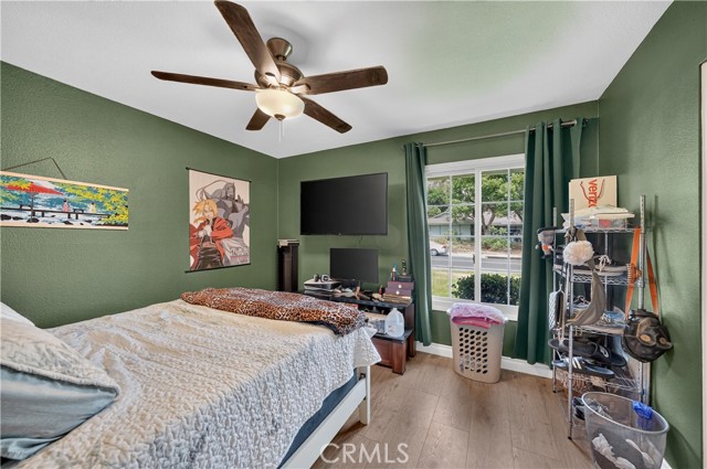 A bedroom with dark green walls, a bed, a ceiling fan, a window, and personal belongings.