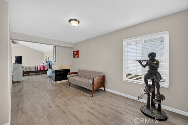 A living room area featuring a mid-century modern sofa, a flute-playing statue, and a double-sided fireplace leading to a bedroom area.