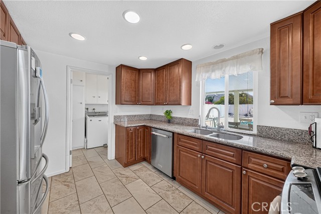 A modern kitchen with cherry wood cabinets, stainless steel appliances, granite countertops, and a view into the laundry room