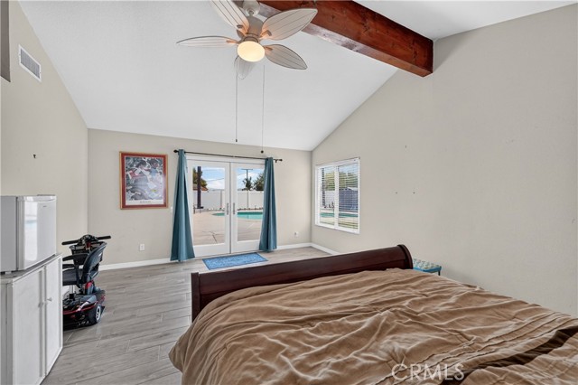 Spacious bedroom with vaulted ceiling, wood beam, ceiling fan, and sliding glass door leading to pool area