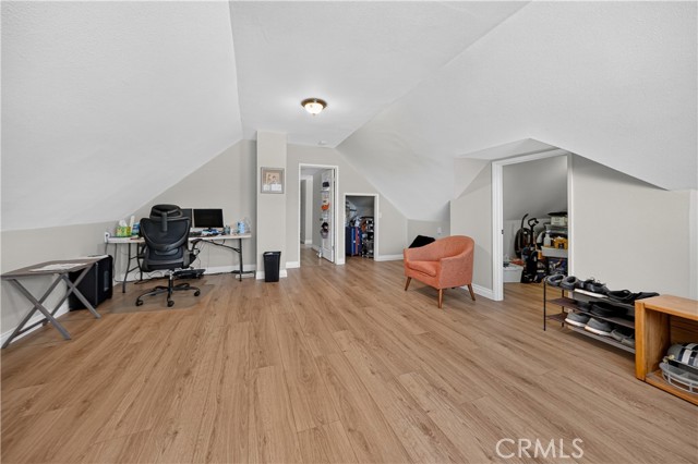 Spacious attic room with sloped ceilings featuring a home office desk, an orange armchair, and storage areas