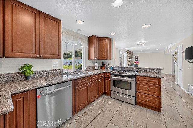 A kitchen with granite countertops, wood cabinets, and stainless steel appliances looking toward the living room.