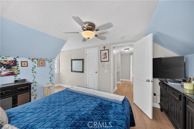 A bedroom with light blue slanted walls, a blue quilt on the bed, a ceiling fan, and dark furniture.