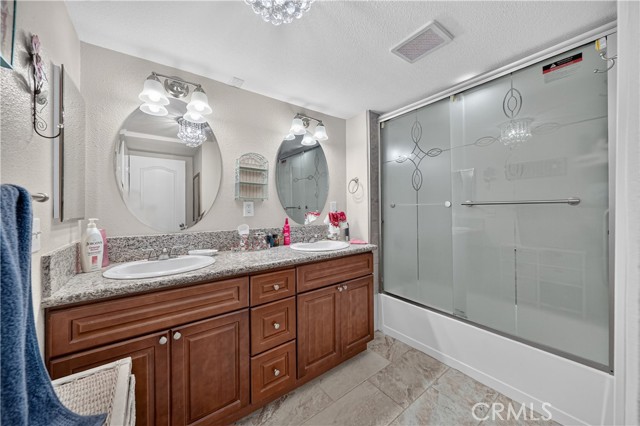 A bathroom with dark wood cabinets, granite countertops, two oval mirrors, and a glass-enclosed shower.