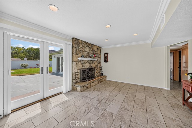 A living room with a large stone fireplace, tile flooring, and glass French doors leading to a patio.
