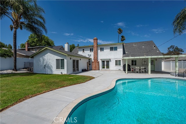 A backyard view showing a white two-story house with a large freeform swimming pool, concrete deck, and green lawn.