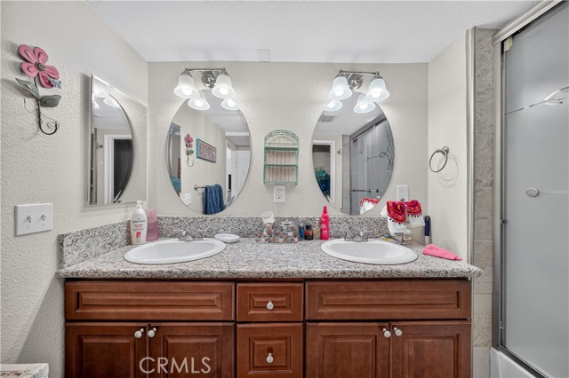 A bathroom vanity with two oval mirrors, two sinks, and wood cabinetry with a granite countertop.