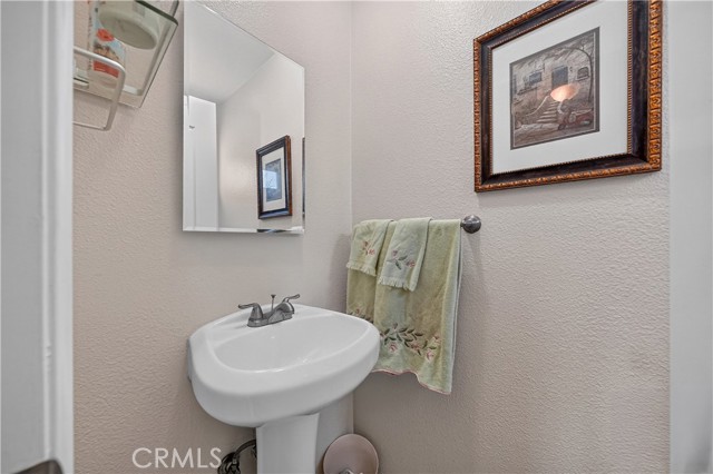 A small bathroom featuring a white pedestal sink, a rectangular mirror, a towel hanging on the wall, and decorative wall art.