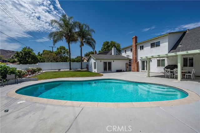 A backyard featuring a kidney-shaped swimming pool, a concrete patio, and a white two-story house.