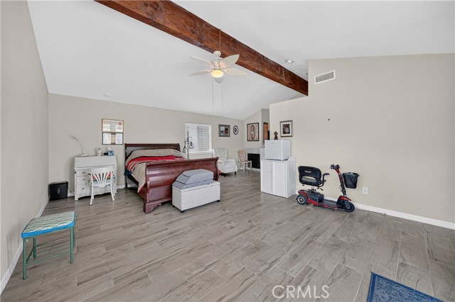 Spacious bedroom featuring a vaulted ceiling with an exposed wood beam, a sled bed, a desk in the corner, and a mobility scooter, with wood-look tile flooring.
