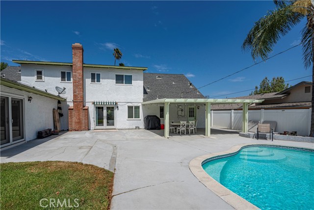 Back exterior of a white stucco house with a swimming pool and covered patio area.