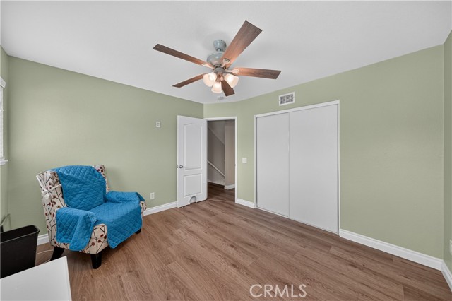 A bedroom with sage green walls, light wood-look flooring, a blue-covered armchair, and a white sliding closet door.