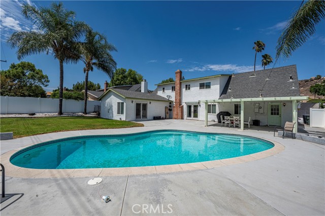 The backyard of a white house featuring a swimming pool, covered patio, and landscaped yard.