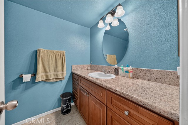 A small bathroom with bright blue walls, a wooden vanity cabinet, granite countertop, and oval mirror.