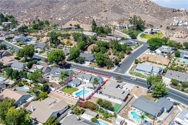 Aerial view showing residential houses in a hilly area with a specific property highlighted by a red dashed line outline including the backyard swimming pool.