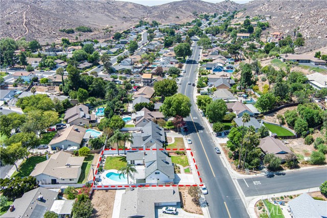 Aerial view of a residential property with a pool, highlighting the lot boundaries in red, set within a suburban neighborhood with hills in the background.