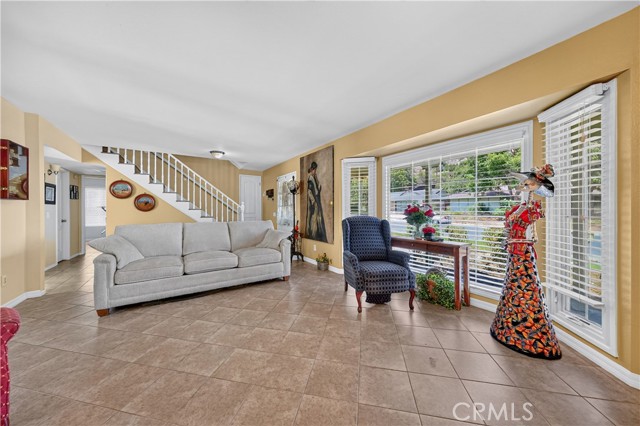 Spacious living room featuring a grey sofa, blue armchair, tiled flooring, a staircase to the upper level, and a large bay window.