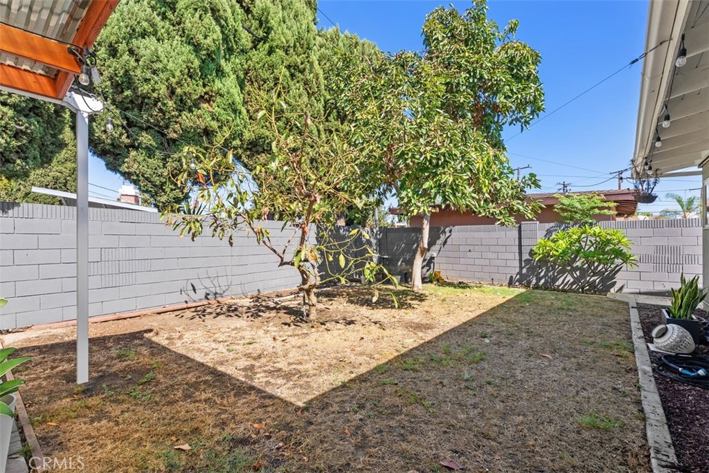 Fenced backyard at 9925 Rutland Avenue with a mature shade tree, dry lawn, and covered patio area.