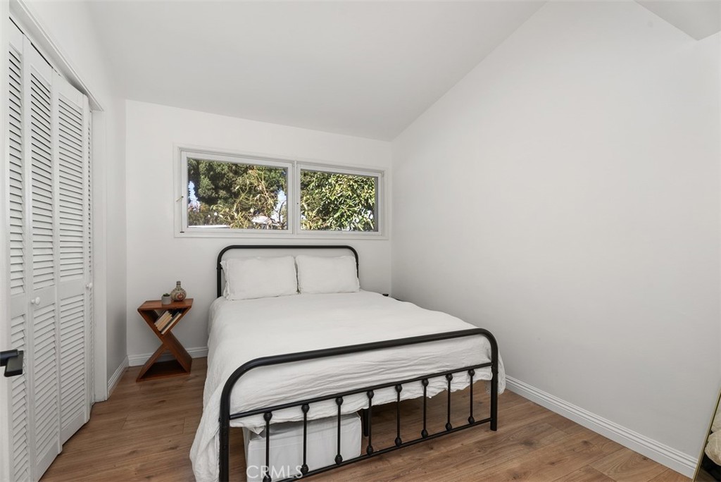 Bedroom at 9925 Rutland Avenue with a black metal bed, white bedding, wood floors, a window, and louvered closet doors.