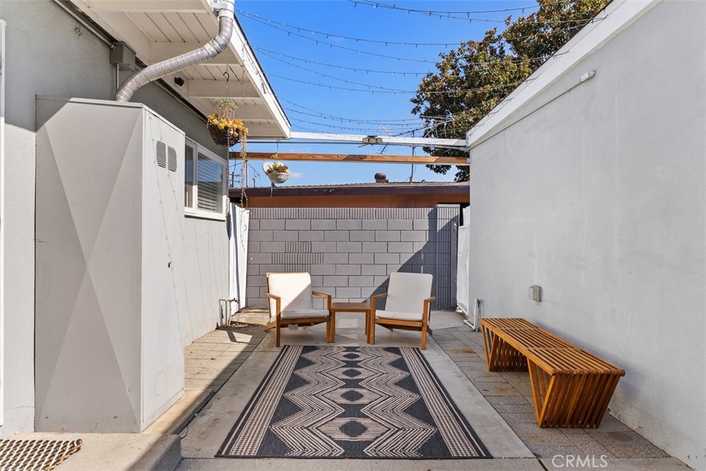 Paved courtyard at 9925 Rutland Avenue with two lounge chairs, a patterned outdoor rug, and a wooden bench between white walls.