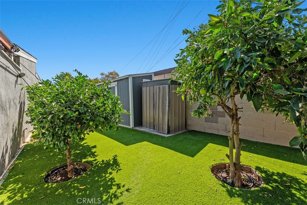Private backyard at 9925 Rutland Avenue with artificial turf, two leafy trees, and a modern gray storage shed.