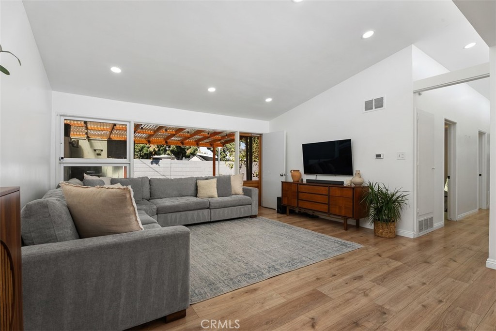 Bright living room at 9925 Rutland Avenue with a gray sectional, large windows overlooking a covered patio, and a TV on a wood console.