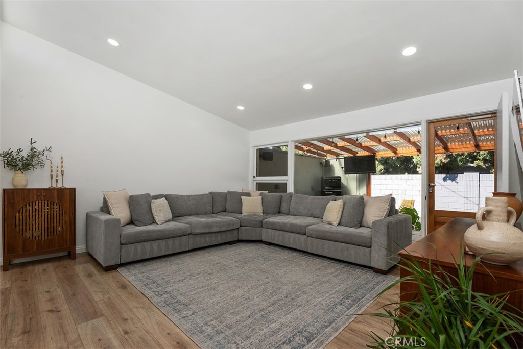 Living room at 9925 Rutland Avenue with a gray L-shaped sectional, area rug, timber flooring, and sliding glass doors opening to a covered patio.
