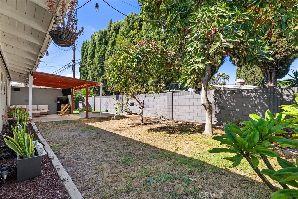 Shaded backyard at 9925 Rutland Avenue with a lawn, mature trees, white block walls, and a covered patio.