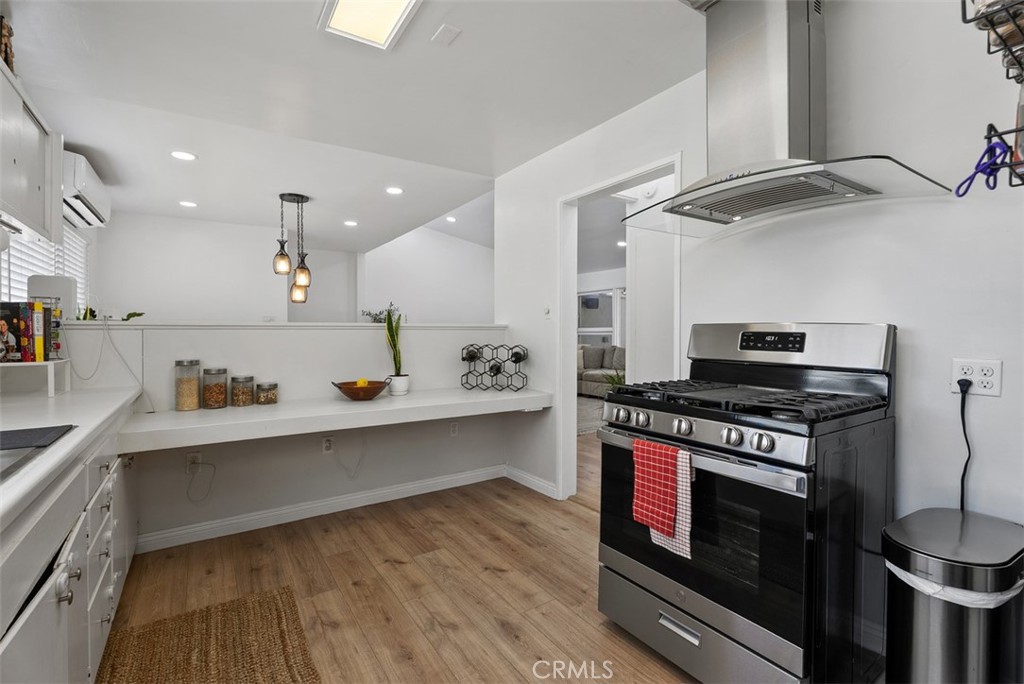 Kitchen at 9925 Rutland Avenue with white cabinets and counters, a black range beneath a stainless steel hood, pendant lights, and wood-look flooring.