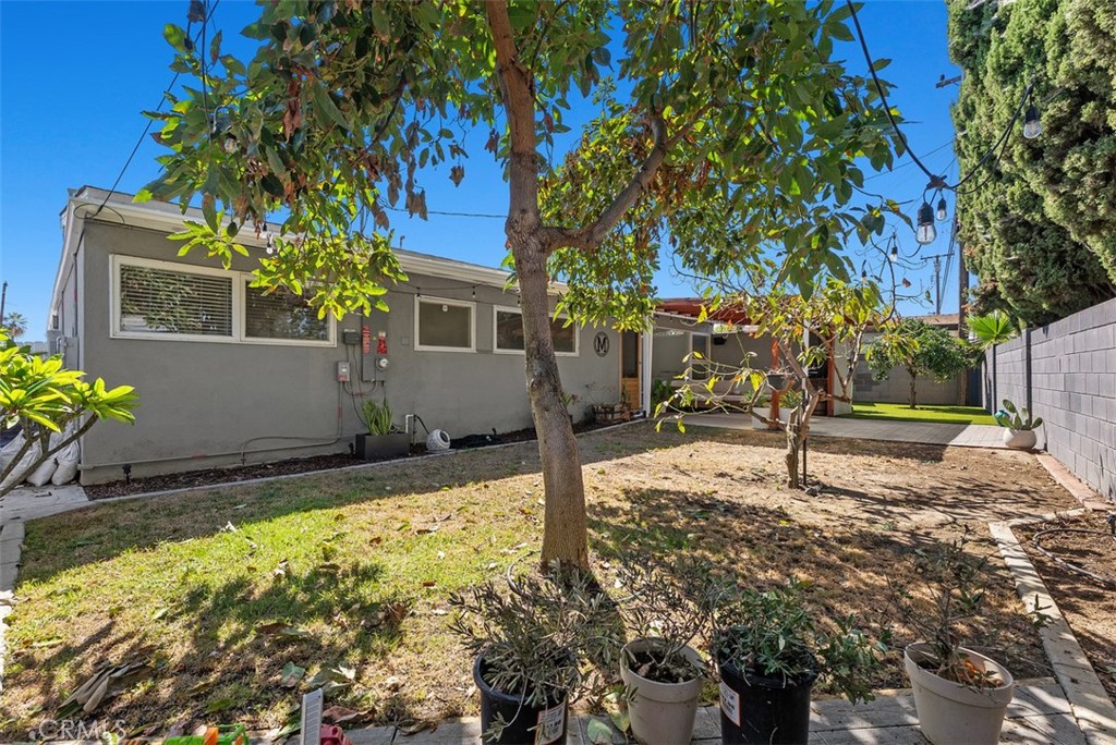 Backyard of 9925 Rutland Avenue, with a lawn, mature shade tree, potted plants, and a single-story home.