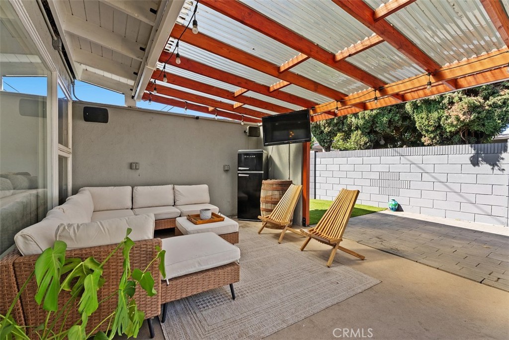 Covered patio at 9925 Rutland Avenue with a wicker sectional, two wooden lounge chairs, an outdoor TV, and a translucent pergola roof.