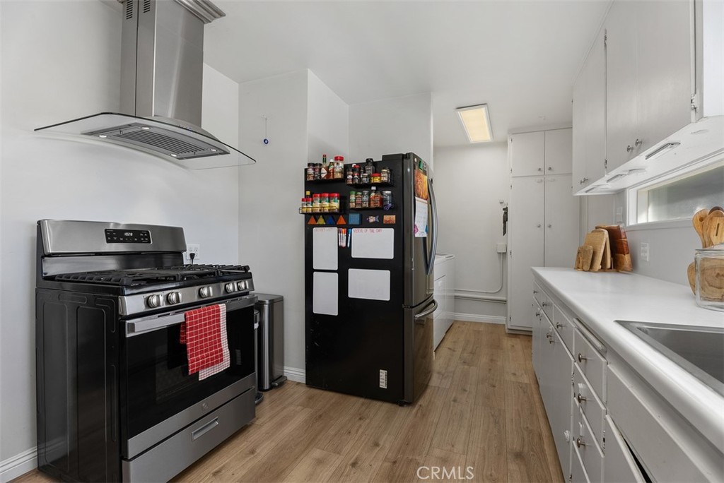 Updated galley kitchen at 9925 Rutland Avenue with black range and refrigerator, white cabinetry, stainless steel range hood, and wood-look flooring.