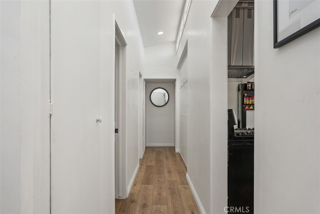 Bright hallway with wood floors, a round mirror at the far end, and a glimpse of the kitchen on the right.