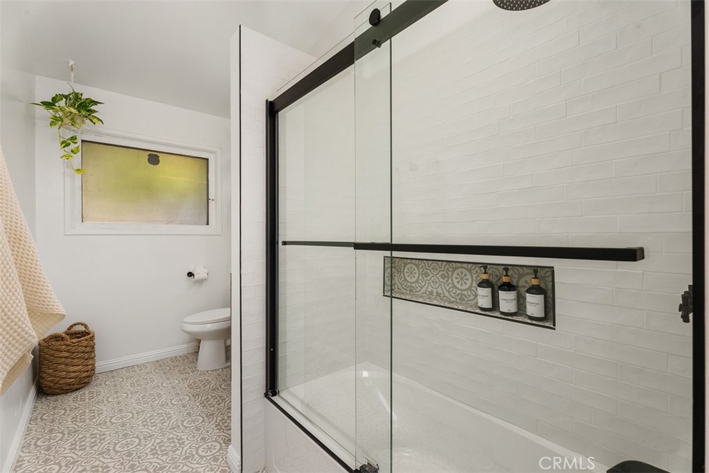 Updated bathroom at 9925 Rutland Avenue with a glass-enclosed shower, white subway tile, patterned floor tile, and a toilet beside a frosted window.