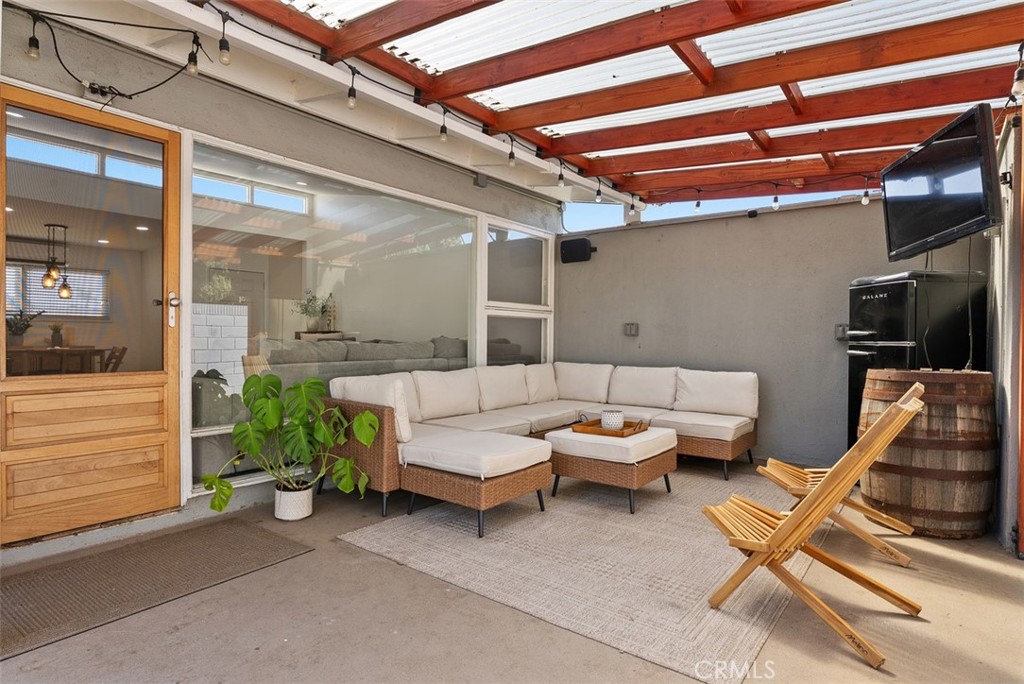 Covered outdoor living area at 9925 Rutland Avenue with a sectional sofa, coffee table, wooden lounge chair, and barrel beneath a red-beamed pergola.