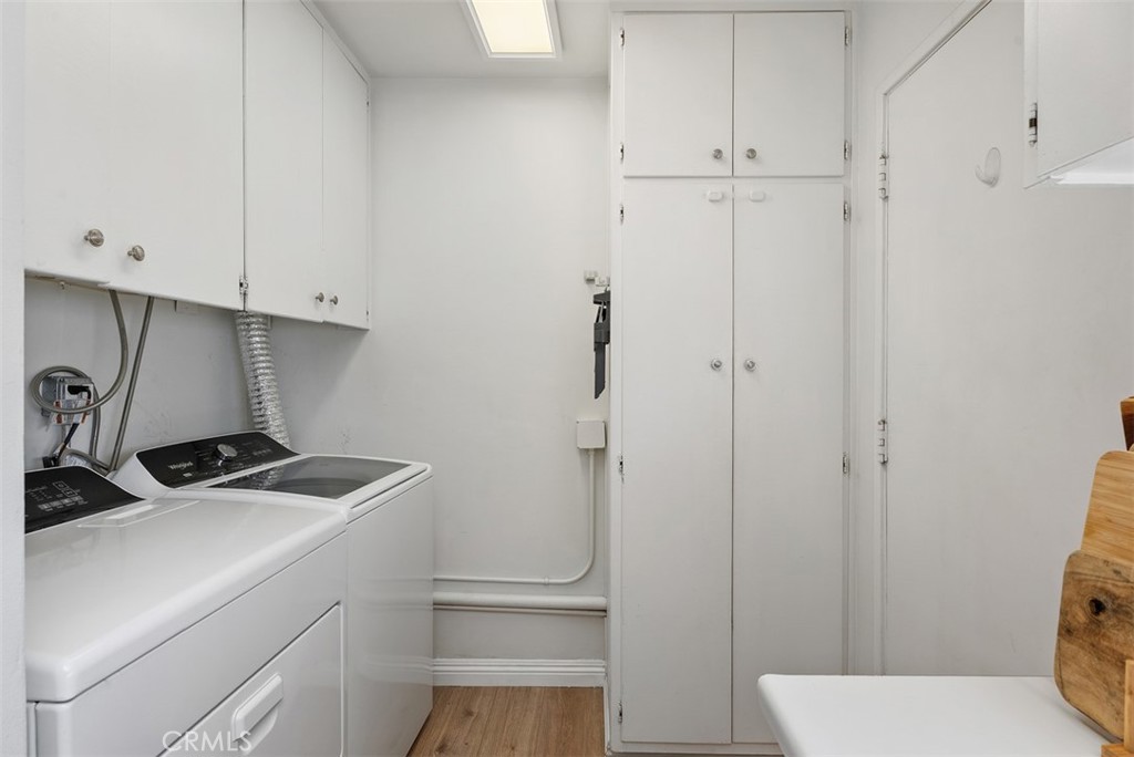 Laundry room at 9925 Rutland Avenue with a washer and dryer, white storage cabinets, and a narrow wood-look floor.