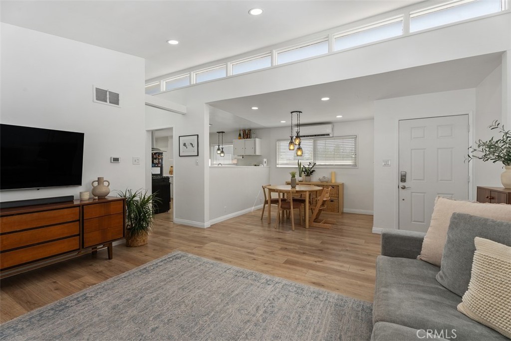 Bright open-plan living and dining area at 9925 Rutland Avenue, with high ceilings, wood floors, a gray sofa, wall-mounted TV, and a dining table beside the kitchen.
