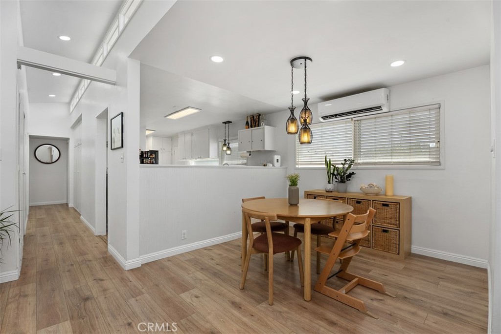 Open dining area at 9925 Rutland Avenue, with a wooden table and chairs beside a woven-front sideboard, overlooking a bright kitchen with a breakfast bar.