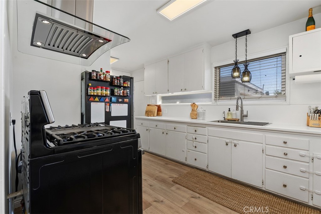 Bright kitchen at 9925 Rutland Avenue with white cabinets, a black range and refrigerator, a farmhouse sink, and wood-look flooring.