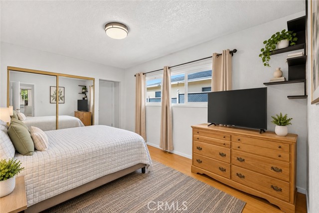 A well-lit bedroom featuring a bed with white bedding, a wooden dresser with a television, and large mirrored closet doors.