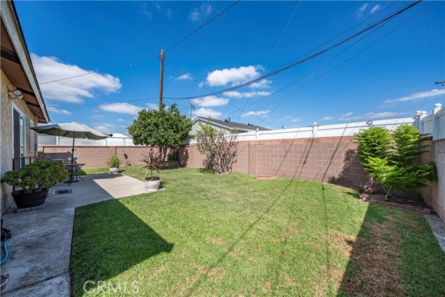 A backyard with a concrete patio area, a green lawn, and a block wall fence.