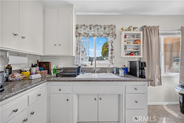 A kitchen with white cabinetry, granite countertops, and a double-basin sink under a window.