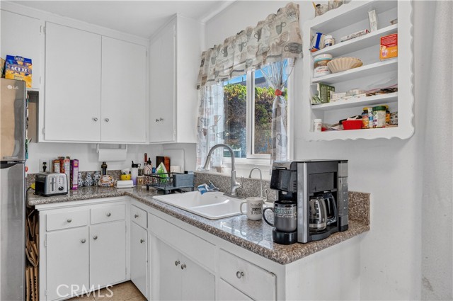 A kitchen sink area with white cabinets, granite-look countertops, and a coffee maker.