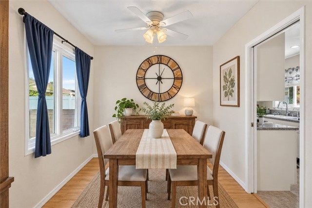 A dining room featuring a wooden table with four chairs, a wall clock, and blue curtains over a window.